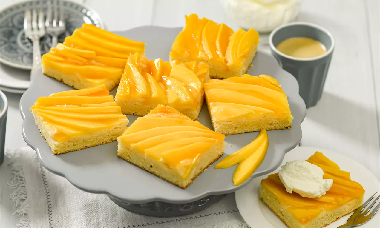 Mangokuchen auf Blech mit goldgelben Mangostücken, saftigem Teig und cremiger Joghurt-Sahne, mit Minzblatt garniert