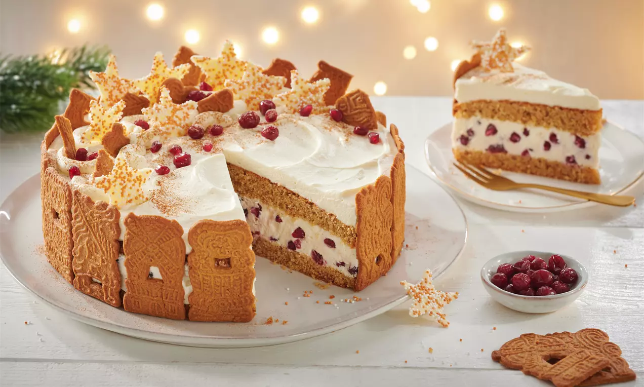 Weihnachtliche Käse-Sahne-Torte mit hellweißem Topping, dekoriert mit roten Beeren, goldenen Sternen und Spekulatius am Rand auf weißem Teller