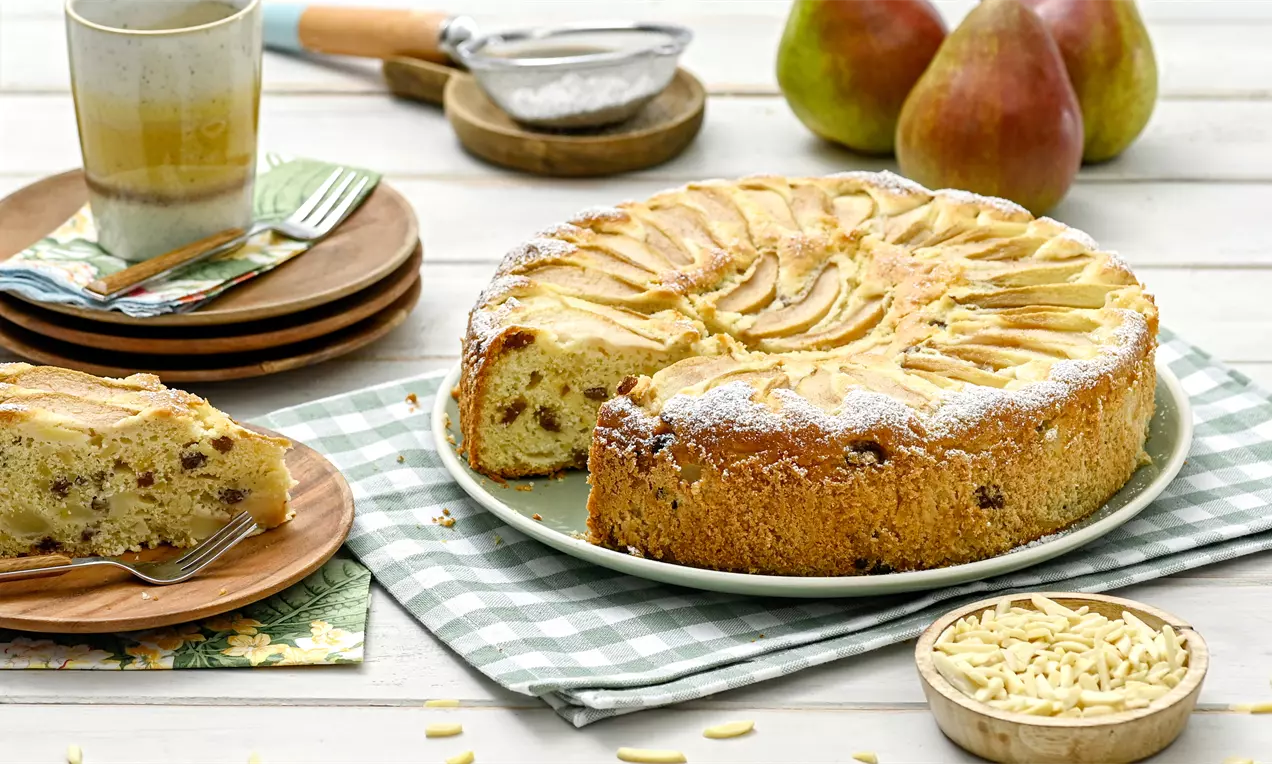 Goldbrauner Birnen-Mandelkuchen mit fächerartig angeordneten Birnenscheiben und Puderzucker auf grün kariertem Tuch serviert