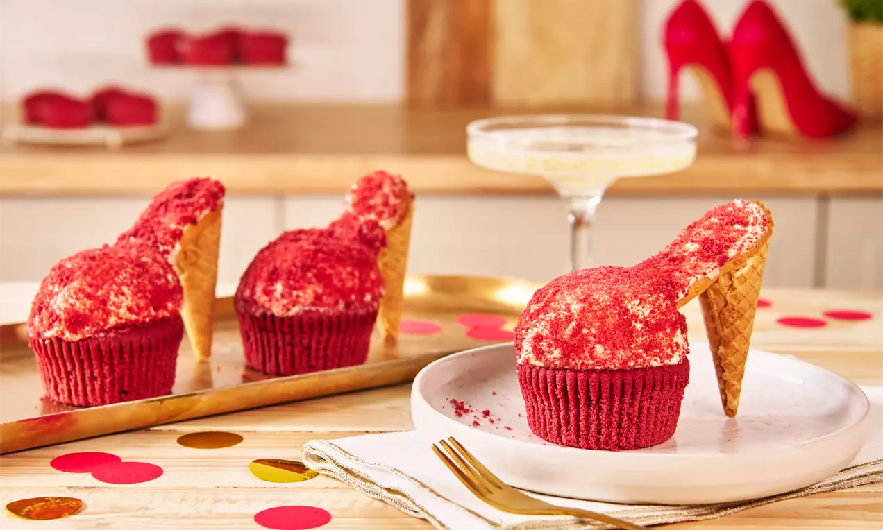 Rote Cupcakes mit Keksen als High-Heel-Dekoration, bestäubt mit roten Krümeln, auf Tellern und Tabletts mit goldenen und roten Akzenten