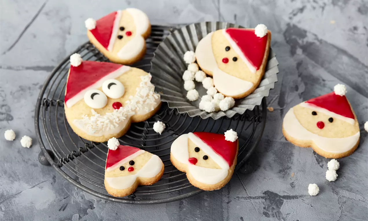 Herzförmige Weihnachtsmann-Plätzchen mit rotem Zuckerguss und weißer Glasur auf einem schwarzen Gitter mit Kokosflocken dekoriert
