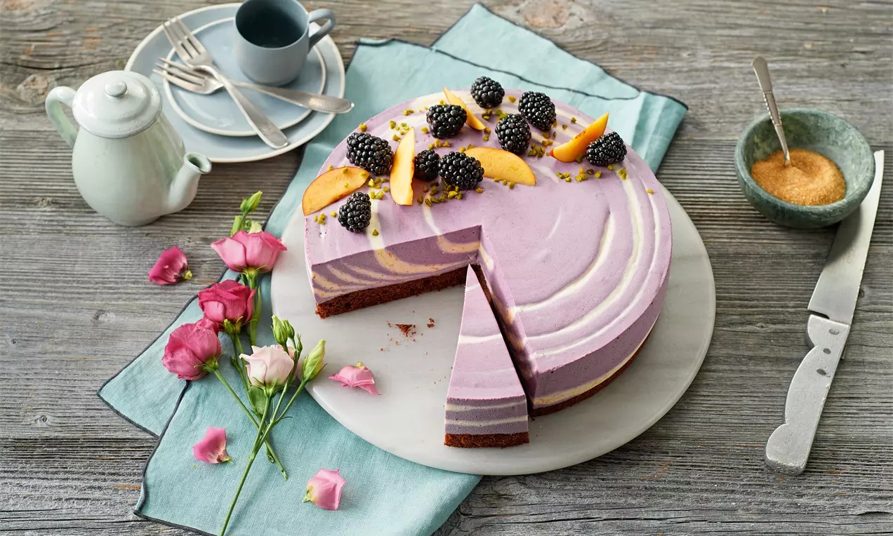 Brombeer-Pfirsich-Käsesahne-Torte mit Zebrakuchen-Optik, dunklem Boden, weißer Quark-Sahne, lila Brombeeren und orange Pfirsichscheiben