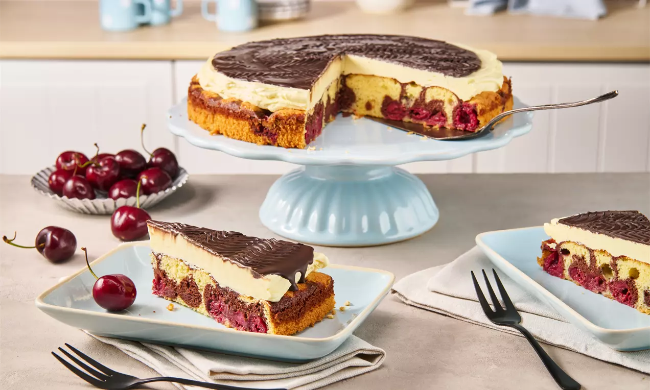 Donauwelle mit hellem und braunem Teig, saftigen Kirschen, heller Creme und dunkler Schokoglasur auf einer blauen Tortenplatte