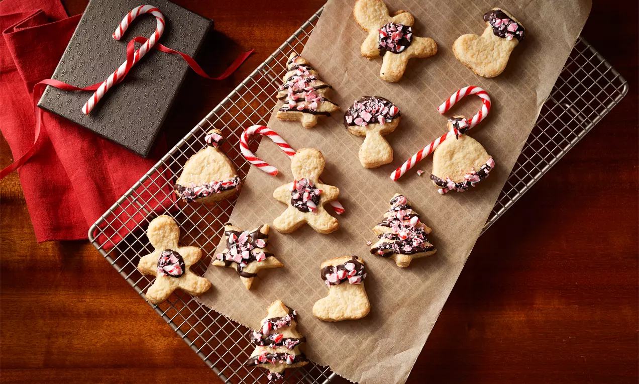 Weihnachtliche Crème-fraîche-Plätzchen in Form von Figuren, teils mit dunkler Glasur und roten Zuckerstücken auf braunem Backpapier