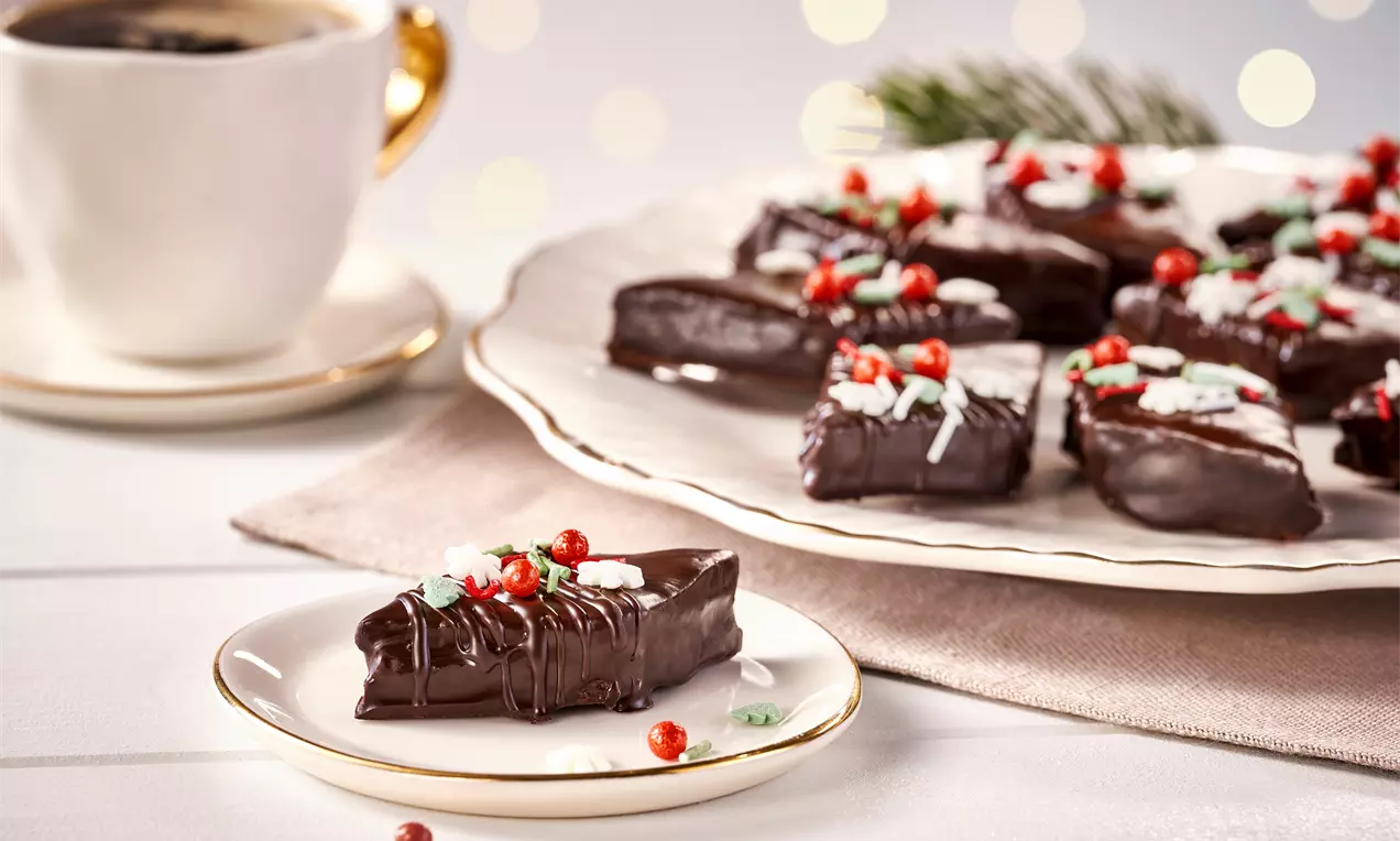 Rechteckige Sacher Plätzchen mit glänzender Schokoladenglasur, verziert mit roten Deko-Perlen und bunten Streuseln auf Porzellantellern