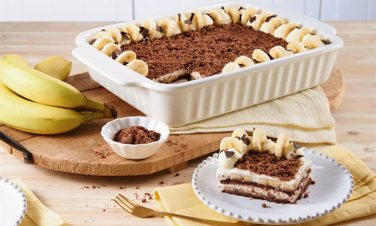 Maulwurfkuchen mit lockerer Schokoladenkrümeldecke, Bananenscheibenrand und cremiger Füllung in weißer rechteckiger Form auf Holzbrett