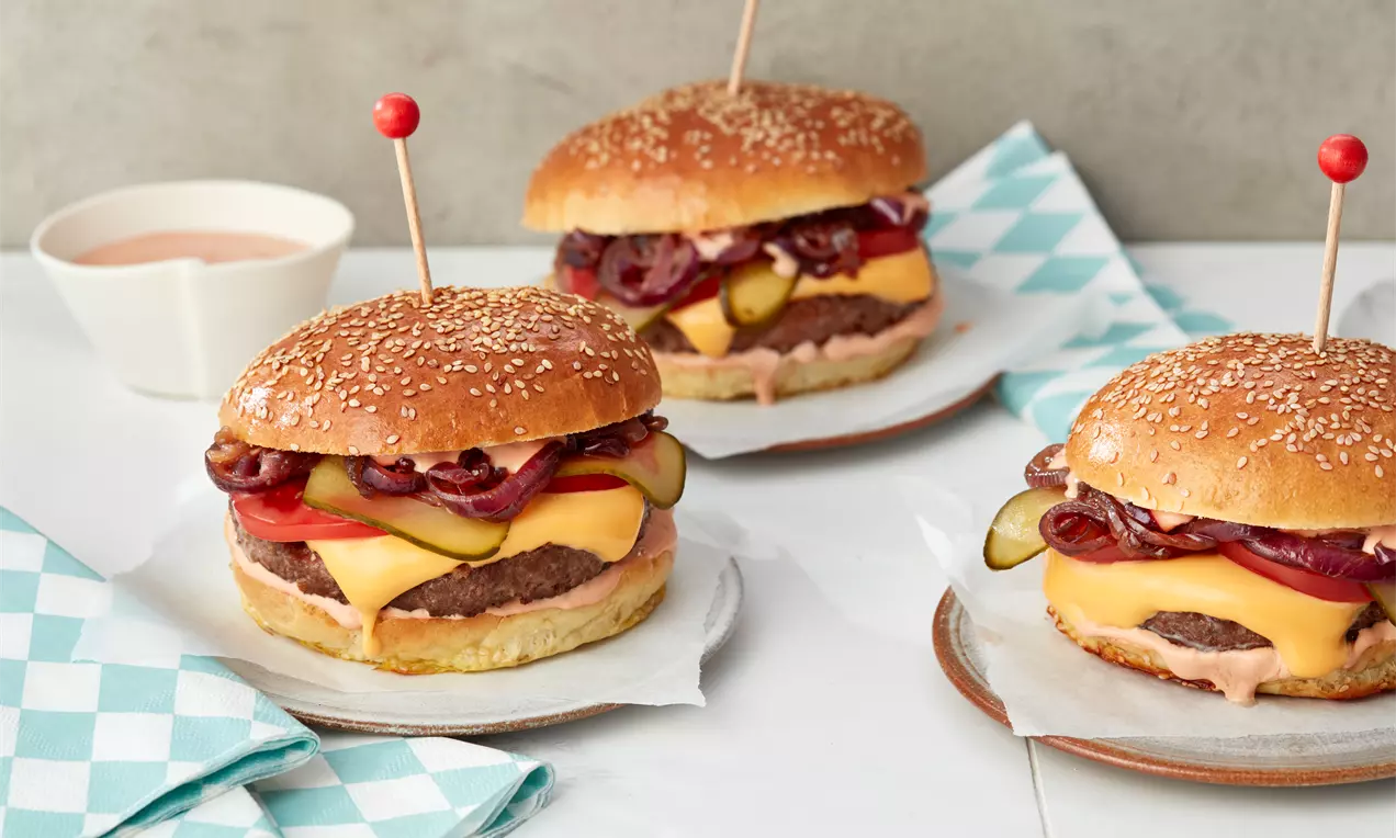 Cheeseburger mit goldbraunem Sesambrötchen, geschmolzenem Käse, saftigem Patty, Röstzwiebeln und Gurken auf weißem Papier angerichtet