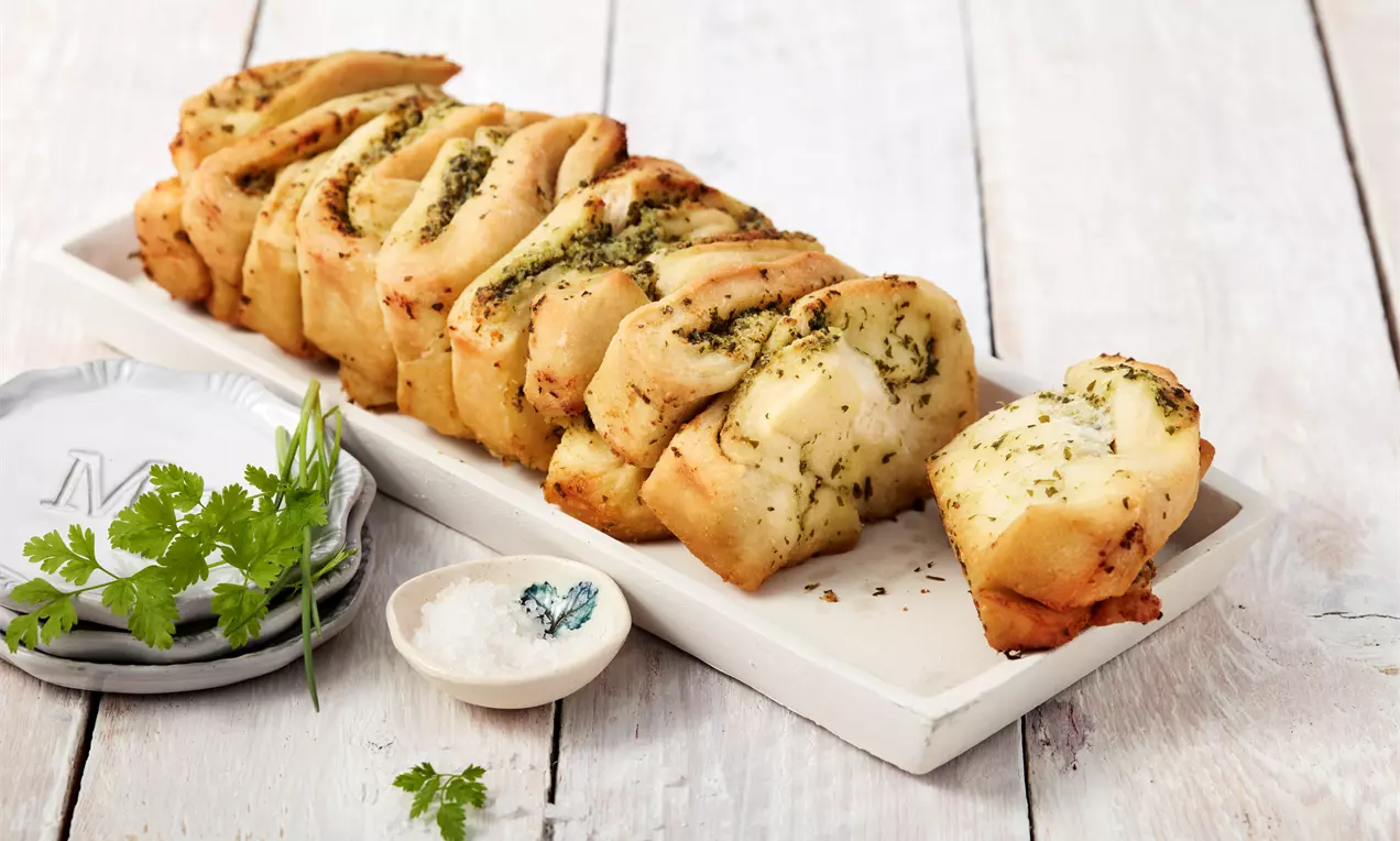 Kräuterzupfbrot mit goldbrauner Kruste und grünen Kräutern, zupfbare Stücke mit butterglänzender Füllung auf Holzbrett serviert