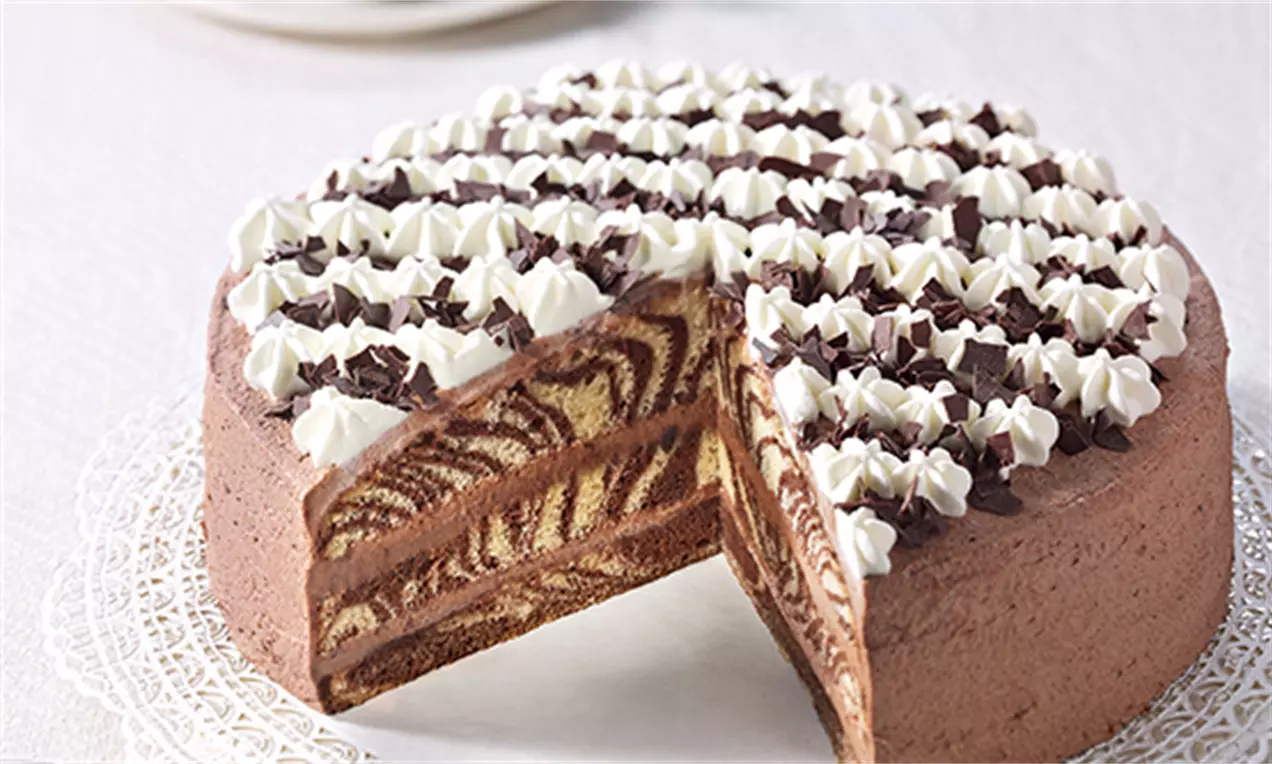 Kreisrunde Zebra-Torte mit spiralförmigem Schokoteigmuster, dekoriert mit Sahnetupfen und Schokoraspeln, auf Tortenspitze angerichtet