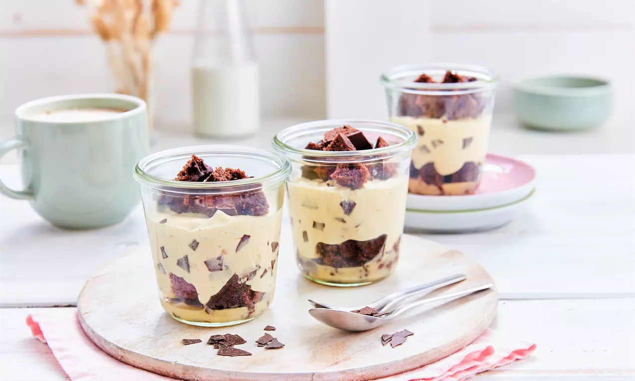 Eierlikör-Mousse in kleinen Gläsern, hellgelb cremig mit dunklen Brownie-Stücken und Schokosplittern auf einem Holzbrett angerichtet