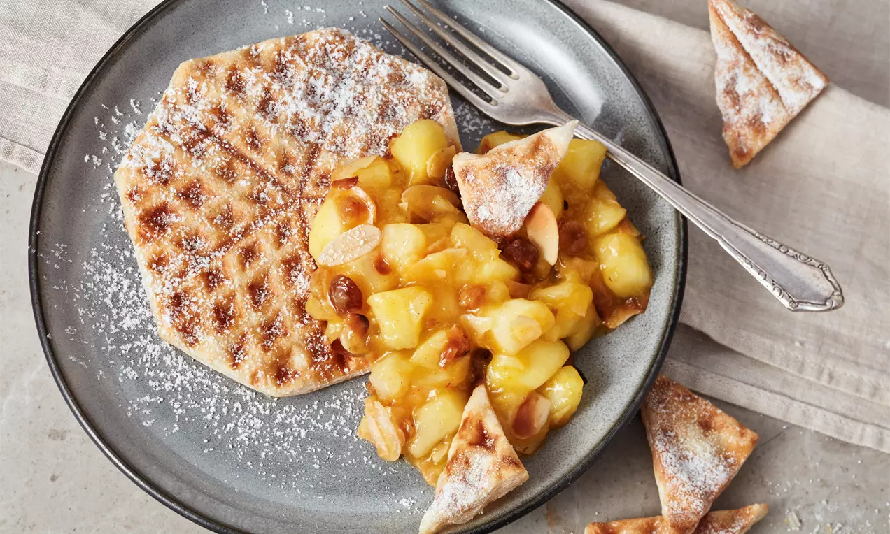 Goldbraune Blätterteigwaffel mit zartem Puderzucker bestäubt, serviert mit fruchtigem Apfelkompott und dekorativen Blätterteigdreiecken