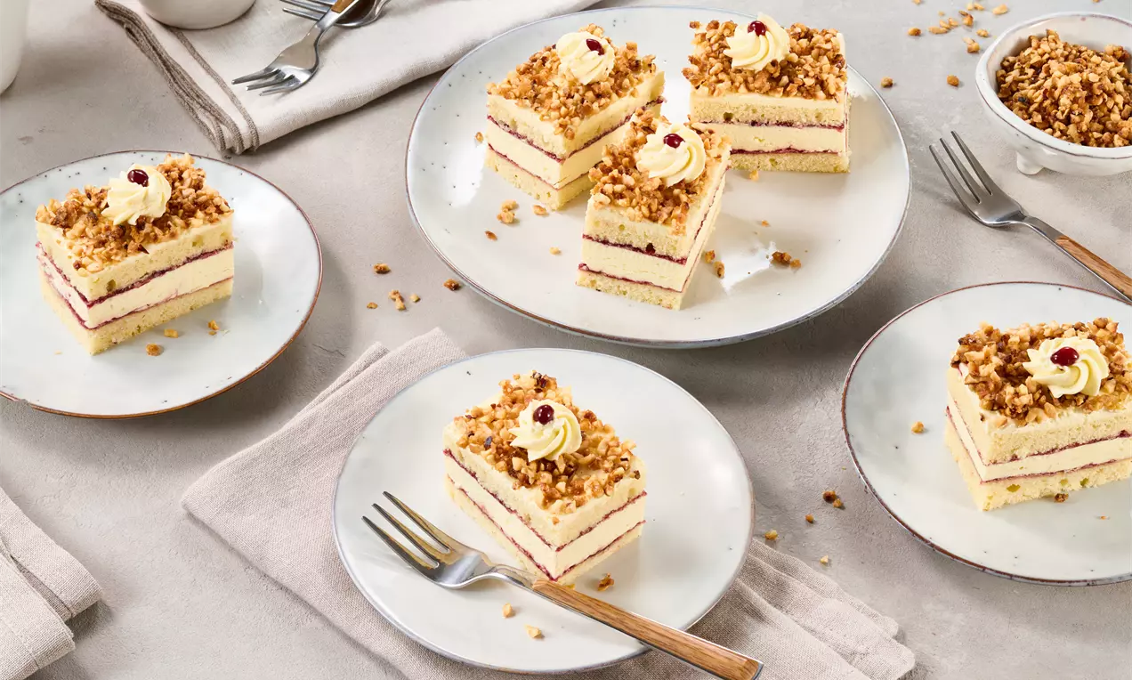 Rechteckige Frankfurter-Kranz-Schnitten mit gelber Buttercreme, roter Geleefüllung und Krokant, auf weißen Tellern serviert