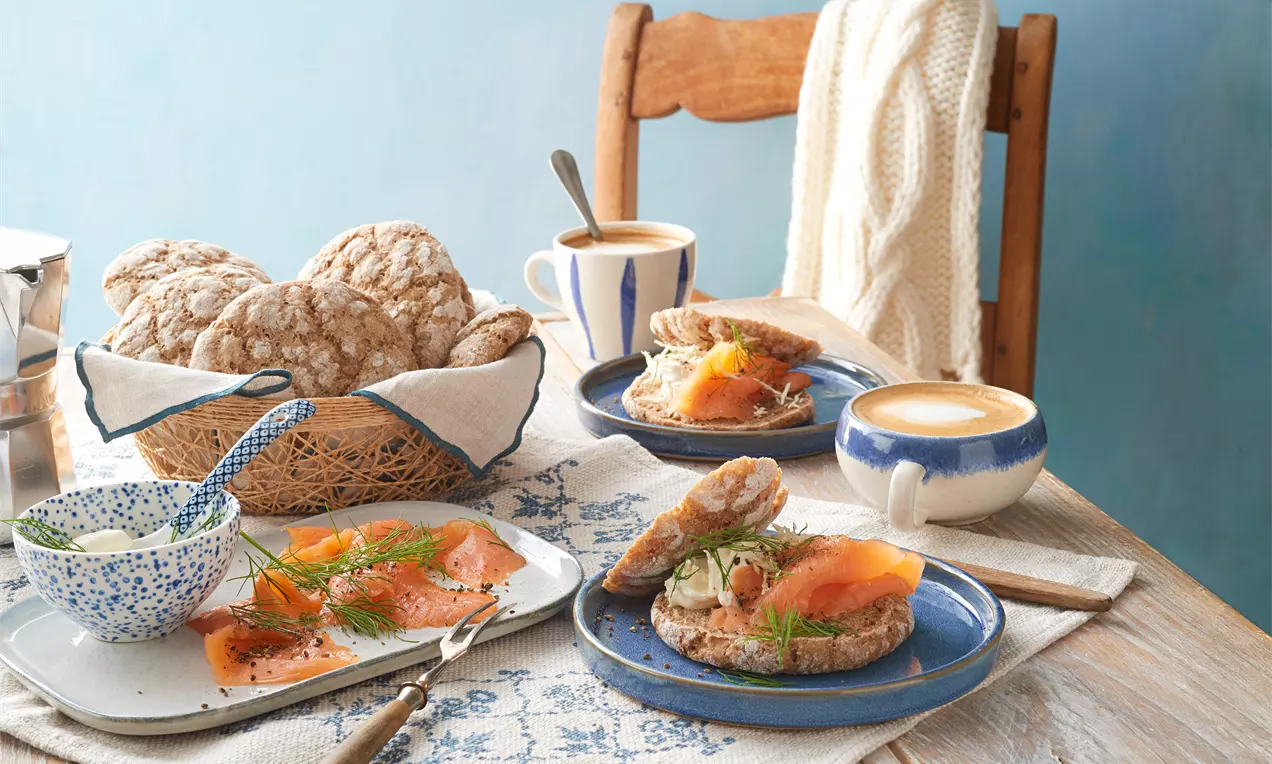 Ruisleipä: saftige finnische Roggenbrötchen mit dunkler Kruste, leicht bemehlt, auf Holzbrett neben Butter und Körnern