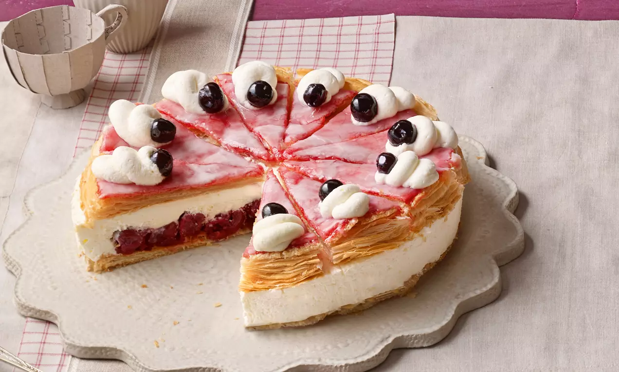 Kreisrunde Holländer-Kirsch-Torte mit Schichten aus Blätterteig, Vanillecreme, Kirschfüllung, rosa Zuckerglasur, Sahnehäubchen und Kirschen
