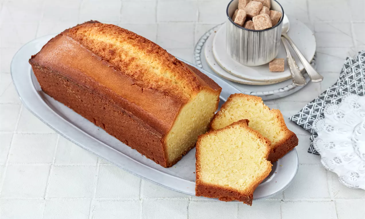 Kastenkuchen mit golden-brauner Kruste, saftigem hellen Inneren und Puderzucker bestäubt auf rustikalem Holzbrett