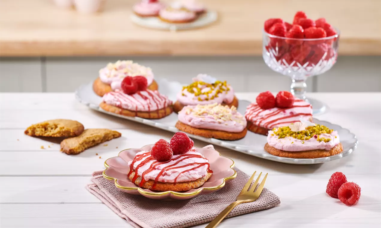 Crumbl Cookies: mehrere große goldbraune Cookies, einer mit rosa Buttercreme, einer mit weißer Glasur und Schokostückchen auf dunklem Teller