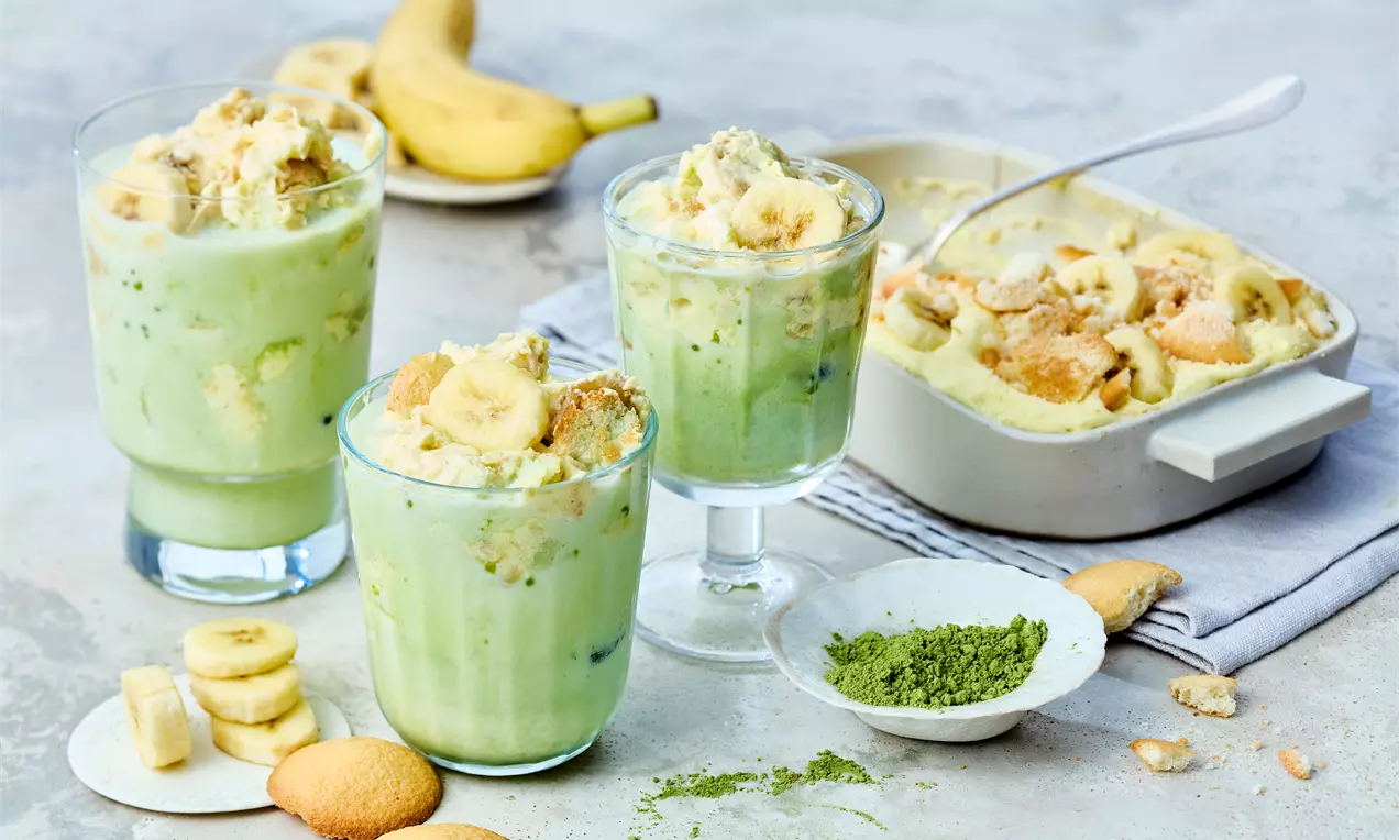 Ein Glas mit geschichtetem Matcha Bananen Pudding, bestehend aus cremiger Paradiescreme, süßen Bananenscheiben, knusprigen Eierplätzchen und von grünem Matcha