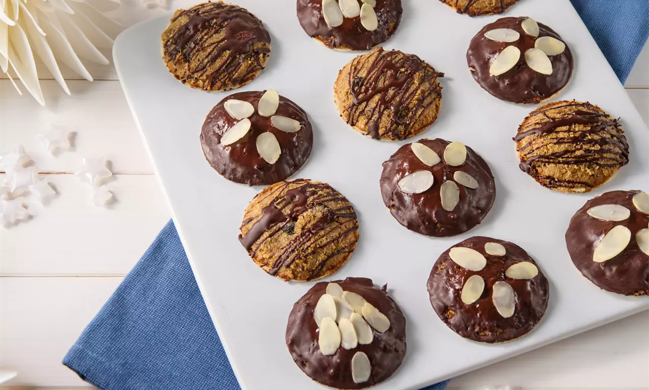 Lebkuchen ohne Zucker in runder Form, teils mit dunkler Schokoladenglasur und Mandelblättchen, auf einem weißen Teller angerichtet