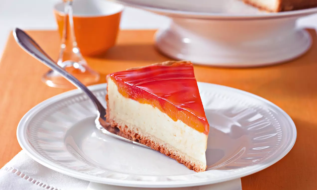 Mandarinen-Käsekuchen mit weißer Füllung auf braunem Boden, bedeckt von glänzendem Pudding und Mandarinenstücken auf einem weißen Teller