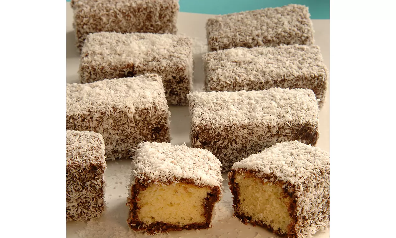 Rechteckige Kuchenstücke mit gelbem Teig, umhüllt von Schokoladenglasur und Kokosraspeln, verteilt auf einem weißen Teller