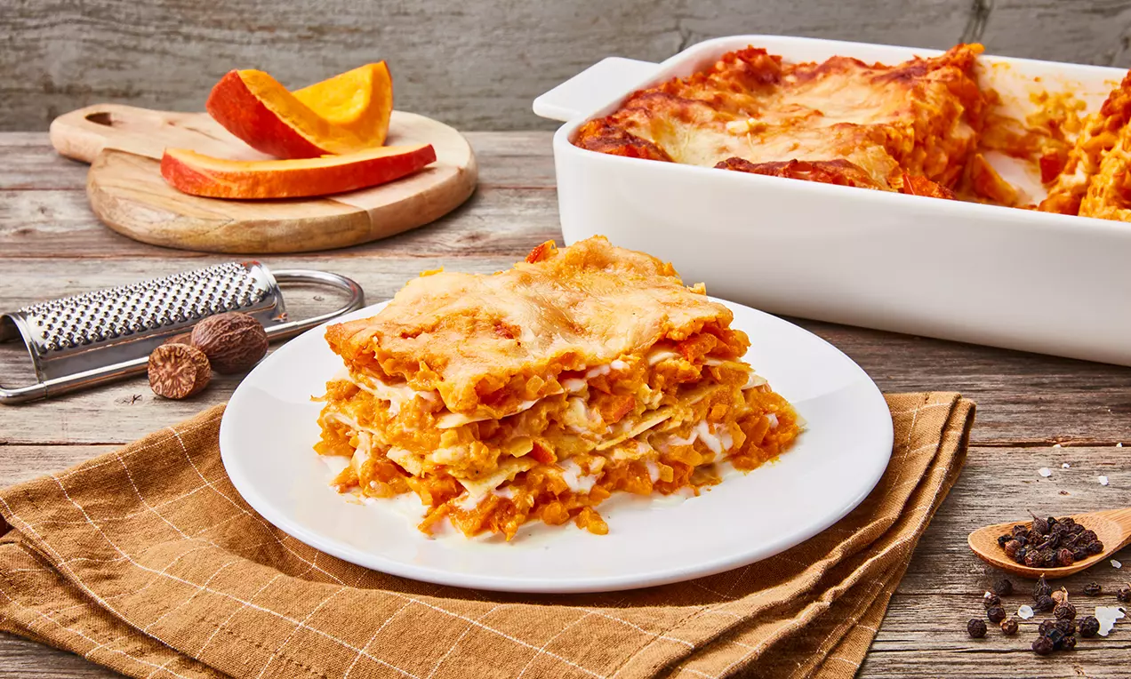 Schichtweise Lasagne mit orangefarbener Kürbis-Tomaten-Füllung und goldbrauner Käsekruste auf einem weißen Teller angerichtet