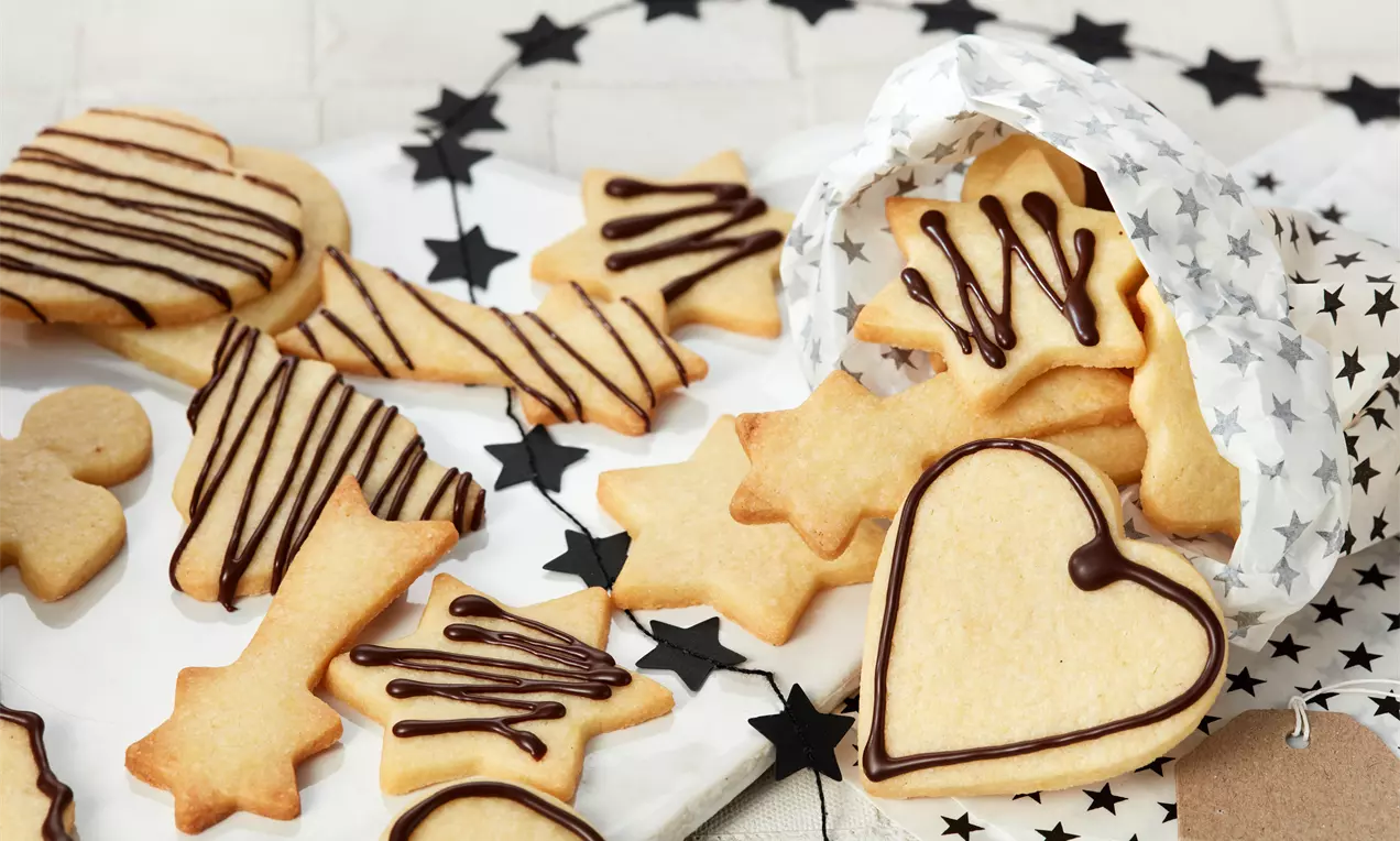 Plätzchen ohne Ei: goldbraune ausgestochene Kekse, teils mit Puderzucker bestäubt, dekorativ auf Backpapier arrangiert