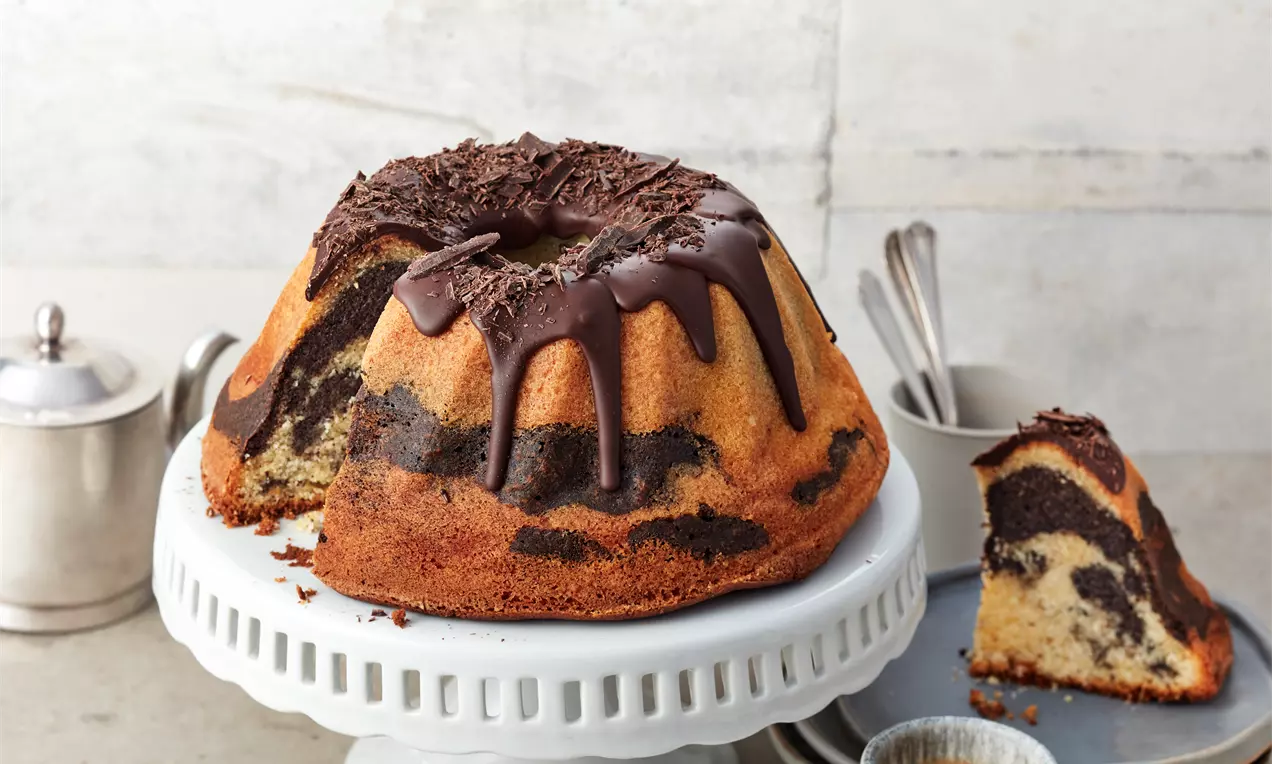 Mohn-Eierlikör-Kuchen in Gugelhupfform mit glänzender Schokoglasur, Mohnfüllung sichtbar und leicht bestäubt, auf weißem Teller