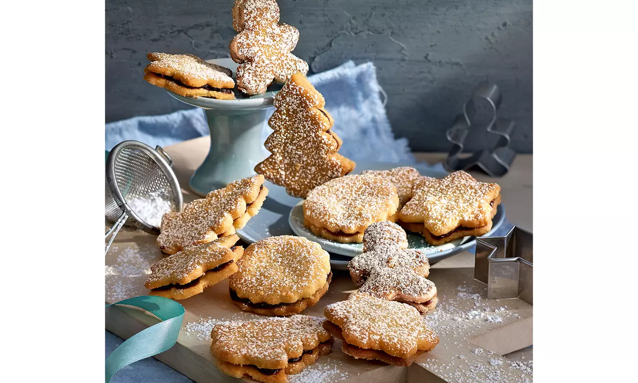 Pflaumenmus-Plätzchen mit goldbraunen, mürben Teigkeksen, glänzender dunkler Pflaumenfüllung und leichtem Puderzucker auf Teller angerichtet