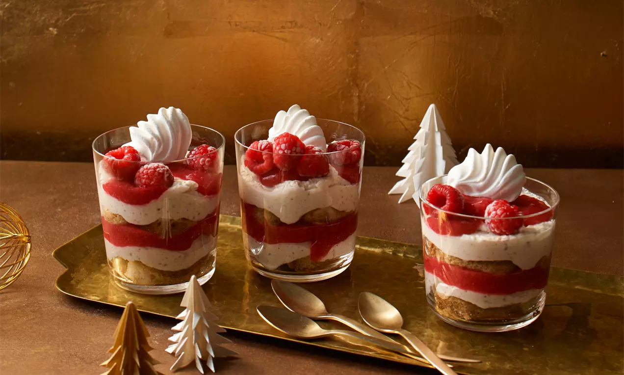 Maronen-Tiramisu im Glas mit geschichteten cremefarbenen und roten Schichten, dekoriert mit Sahnehäubchen und Himbeeren auf goldenem Tablett
