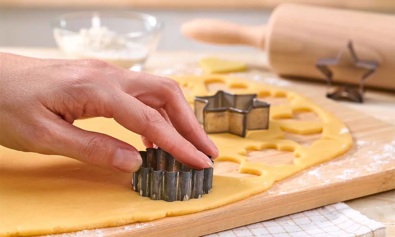 Plätzchenteig auf bemehltem Brett, heller Mürbeteig mit ausgestochenen Sternen, Holzroller, Mehl und Schüssel mit Ei