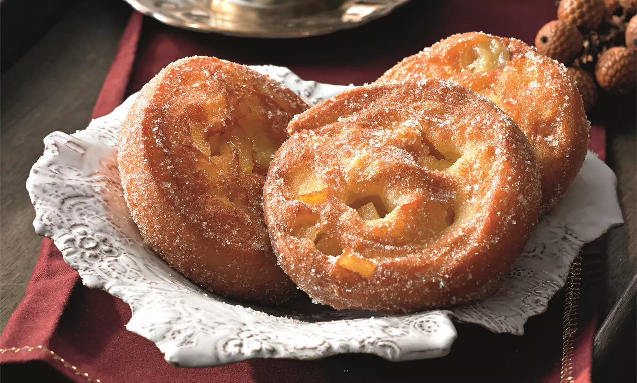 Goldene Apfelberliner mit gezuckerter Oberfläche und leuchtenden Apfelstücken auf zartem Porzellanteller neben einer goldenen Kaffeetasse