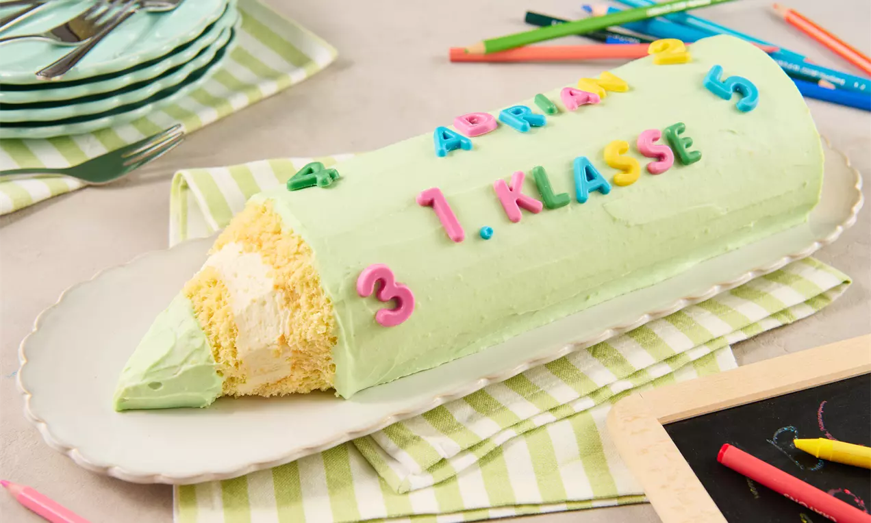 Ein länglicher Kuchen in grüner Glasur, geformt wie ein Buntstift mit freigelegtem hellen Teig, bunten Buchstaben und Zahlen dekoriert
