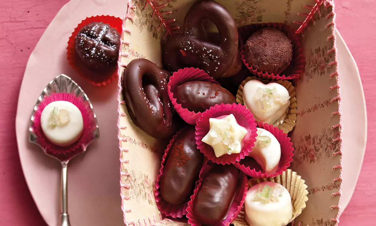 Buntes Marzipan-Konfekt in roten und goldenen Förmchen, glänzend mit Schokolade überzogen, dekoriert mit Kandisstückchen in einer gemusterten Schachtel