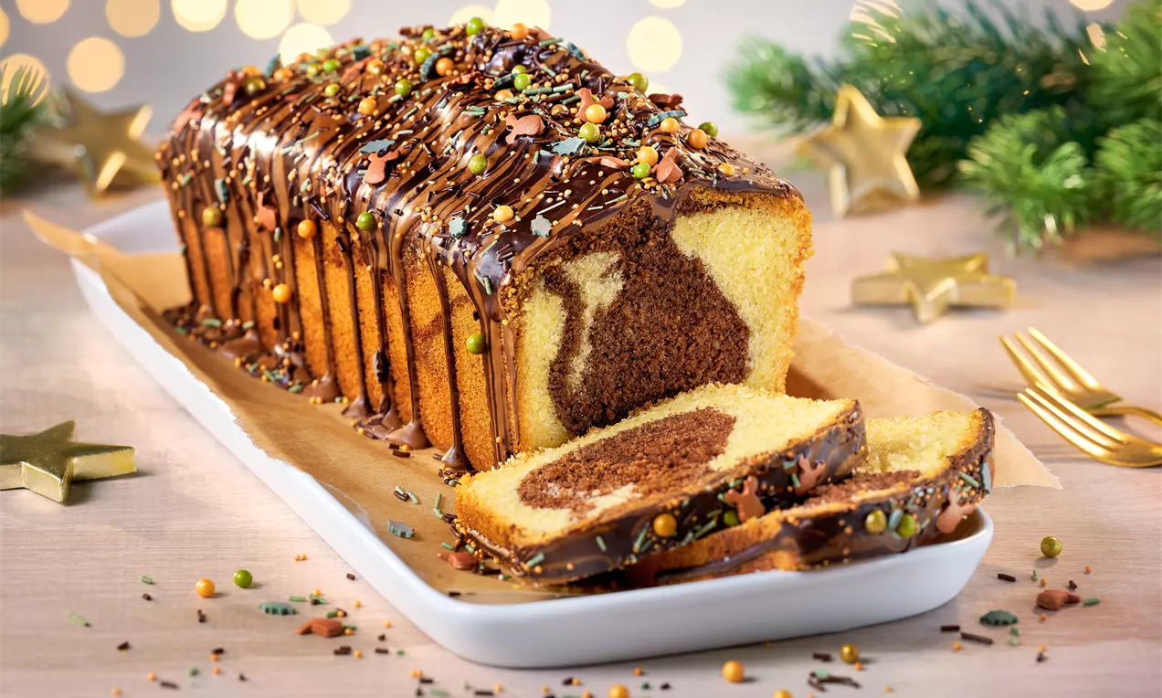 Marmorierter Kastenkuchen mit dunkler Schokoglasur und bunten Streuseln, auf einer weißen Platte mit weihnachtlicher Deko arrangiert