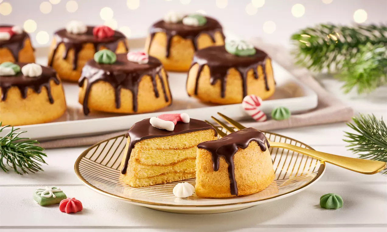 Mini-Baumkuchen-Muffins mit schokoladigem Guss, geschichtetem Inneren, bunt verzierter Oberfläche auf einem Teller mit Tannenzweigen