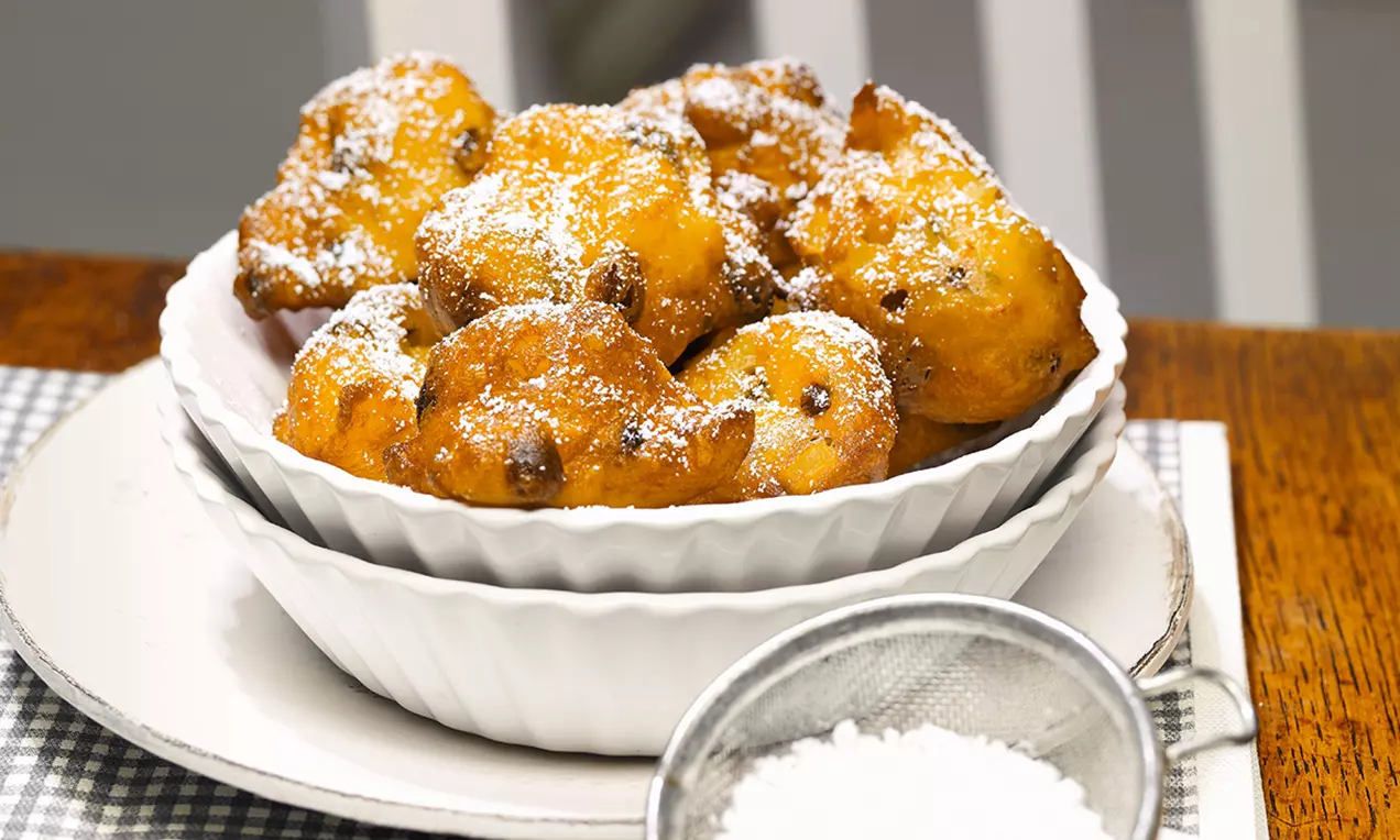 Goldbraune Apfel-Quarkbällchen mit Rosinen, mit feinem Puderzucker bestäubt, in einer weißen Schale auf einem Teller angerichtet