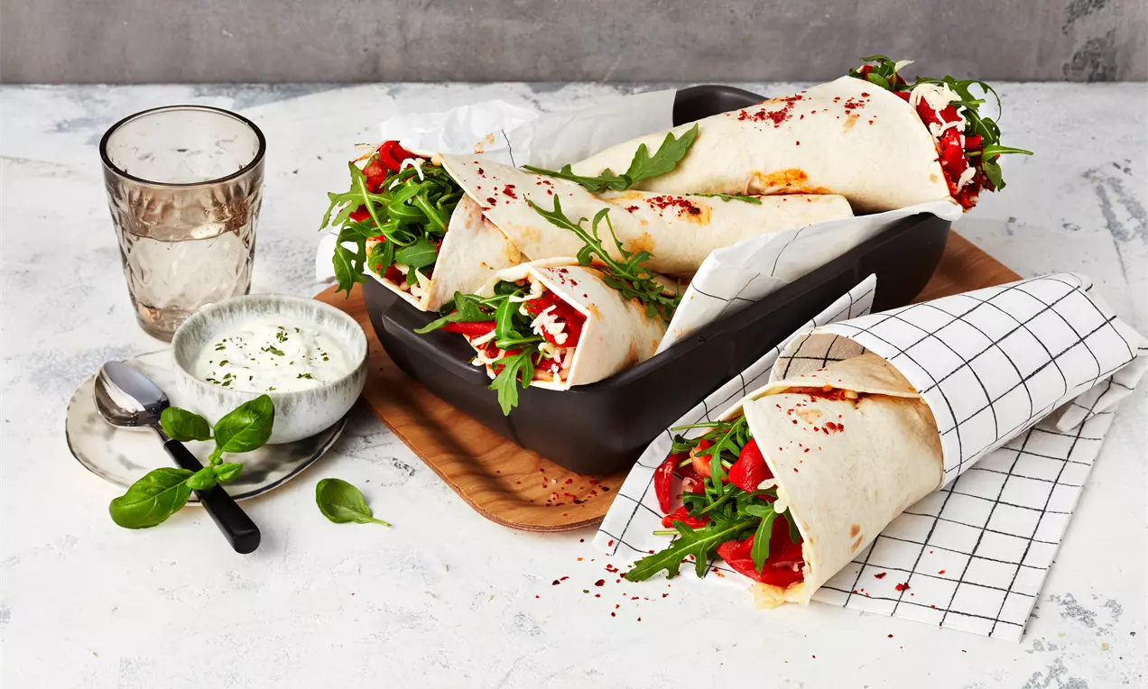 Pizza-Wraps mit knackigem Rucola, roten Paprikastreifen und geschmolzenem Käse, angerichtet in einer dunklen Schale auf Holzbrett