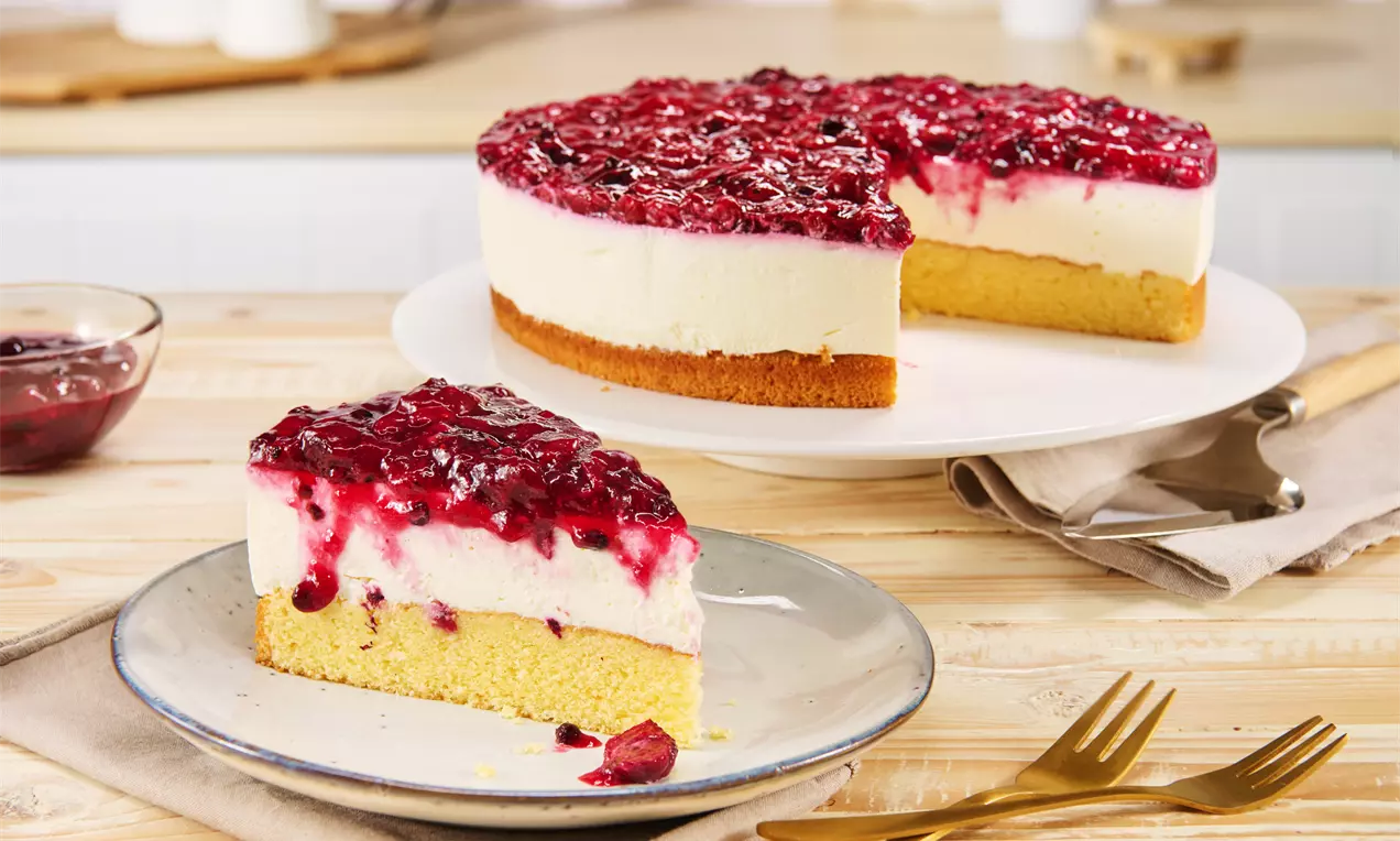 Rote Grütze Torte mit glänzender roter Früchteschicht auf heller Creme und goldenem Biskuitboden, serviert auf weißen Tellern mit goldenen Gabeln