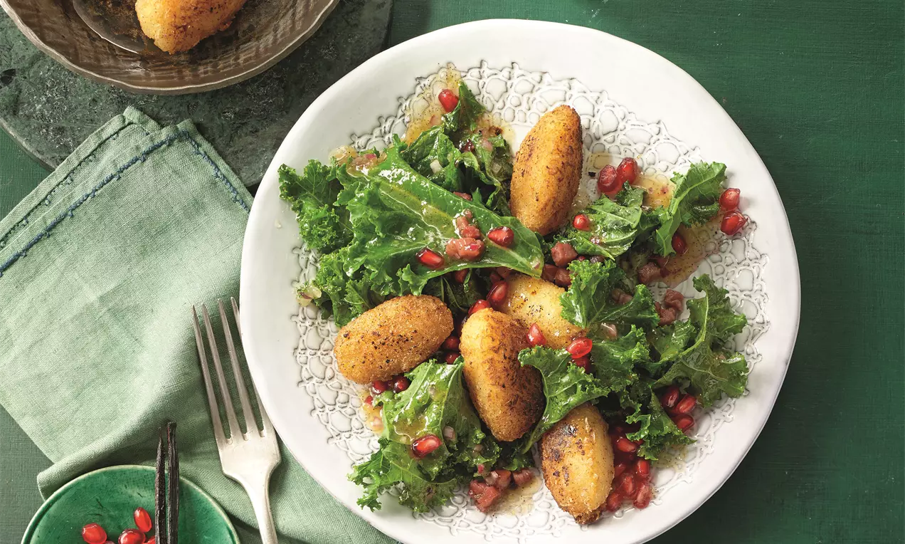 Grünkohlsalat mit gebratenen goldenen Kartoffelnocken, leuchtenden Granatapfelkernen und einem grünen Tuch auf weißem Teller angerichtet