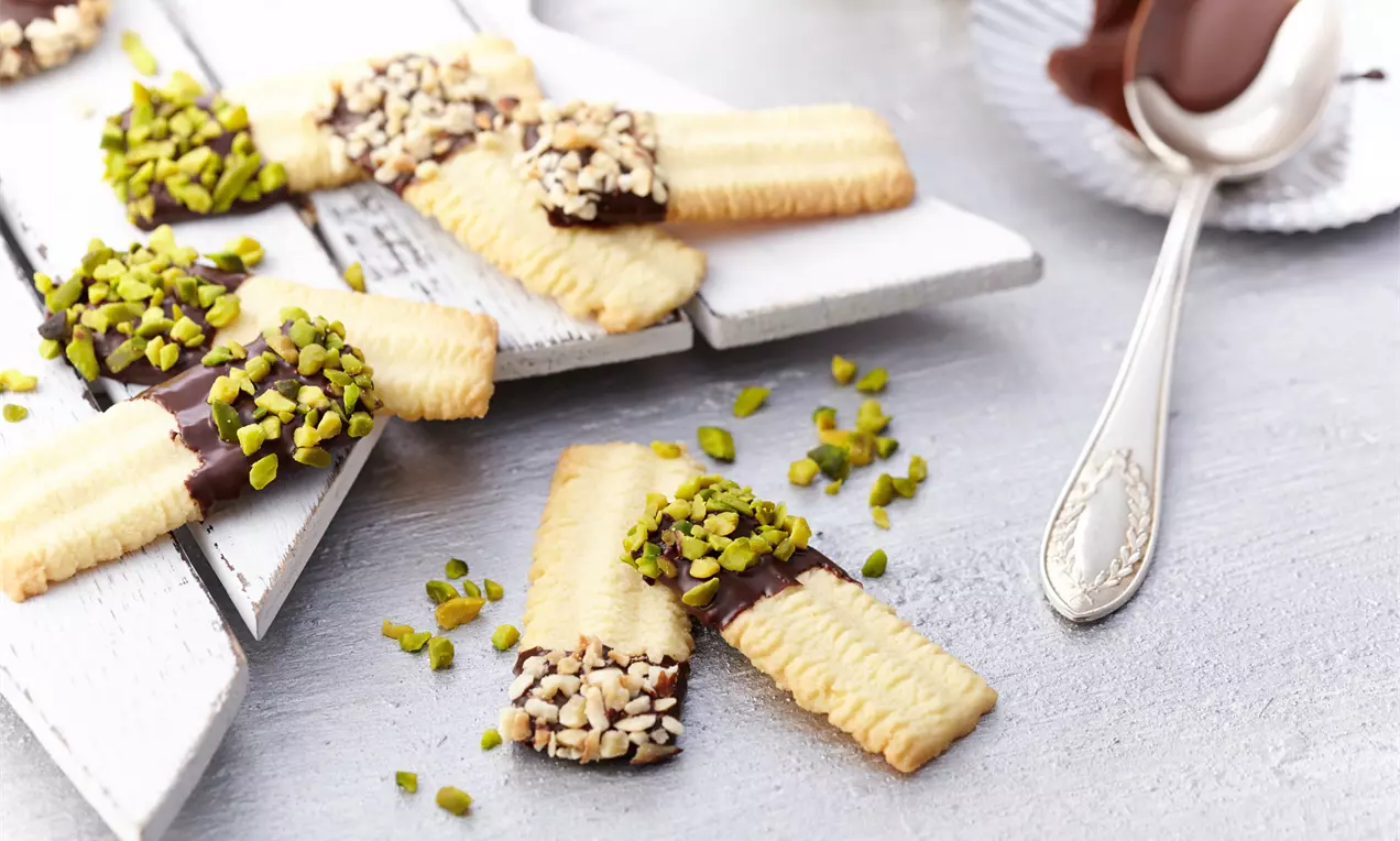 Spritzgebäck goldbraune, gezackte Plätzchen aus dem Fleischwolf auf weißem Porzellanteller, bestäubt mit Puderzucker auf Holzbrett