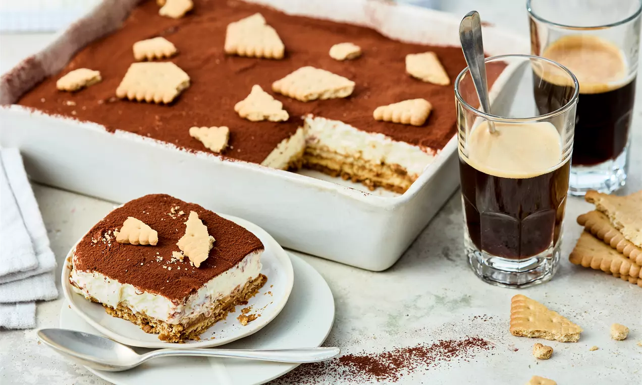 Butterkeks-Tiramisu mit heller Creme und brauner Kakaoschicht, garniert mit Butterkeksstücken, serviert in einer weißen Form und auf einem Teller