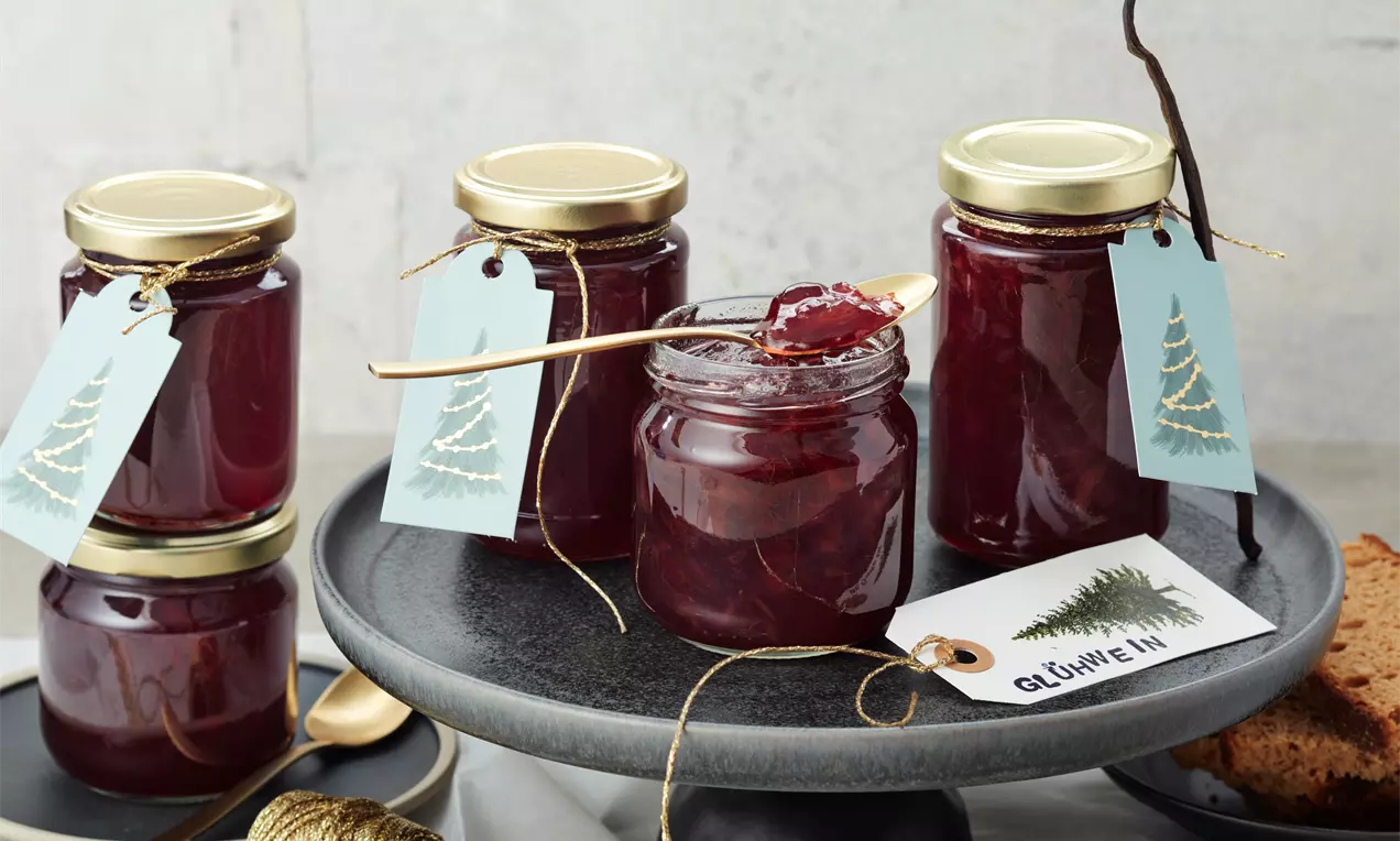 Glühwein-Marmelade in gläsernen Schraubdeckelgläsern mit goldenen Deckeln, tiefrote glänzende Farbe, dekoriert mit hellblauen Geschenkanhängern