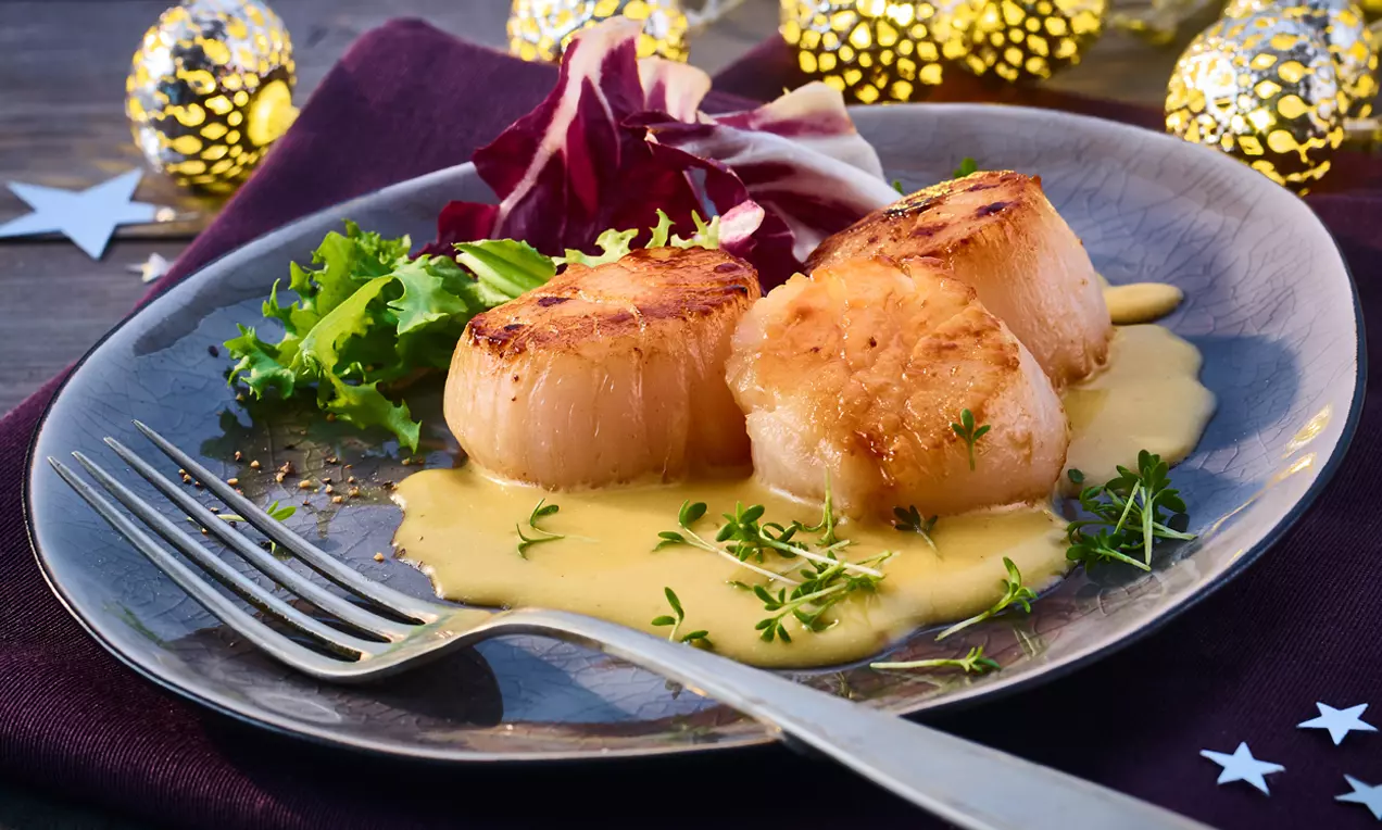 Gebratene Jakobsmuscheln mit goldbrauner Kruste auf cremiger Sanddorn-Crème-fraîche, angerichtet mit frischem Salat und Kresse auf grauem Teller