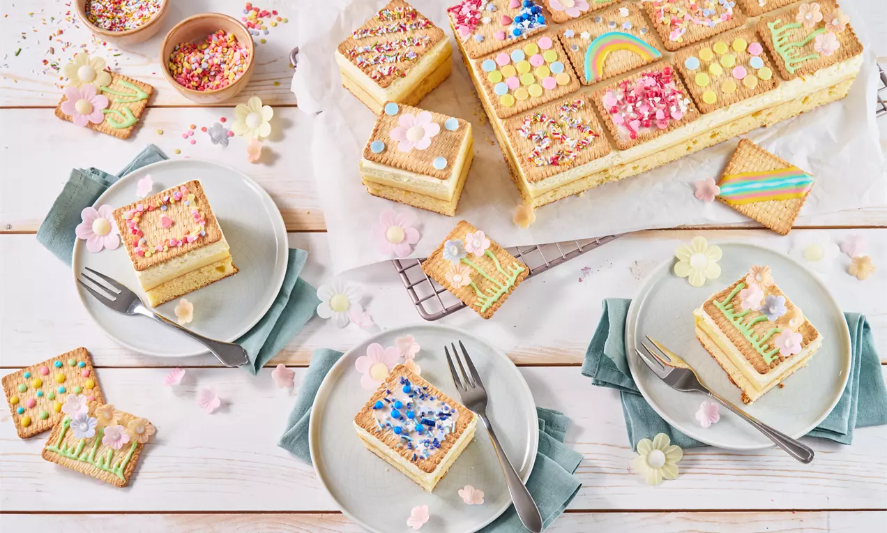 Rechteckiger Butterkekskuchen mit bunter Verzierung aus Zuckerguss und Dekorstreuseln auf Holzplatte, in Quadrate geschnitten, auf Tellern serviert