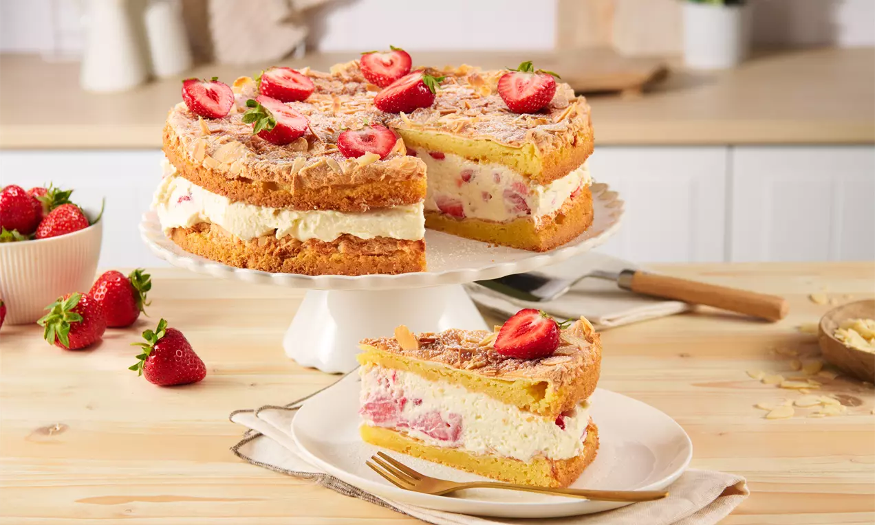 Erdbeer-Baiser-Torte mit goldbraunem Biskuit, weißer Sahnefüllung, frischen Erdbeerstücken und Baiserhaube auf einer Tortenplatte angerichtet
