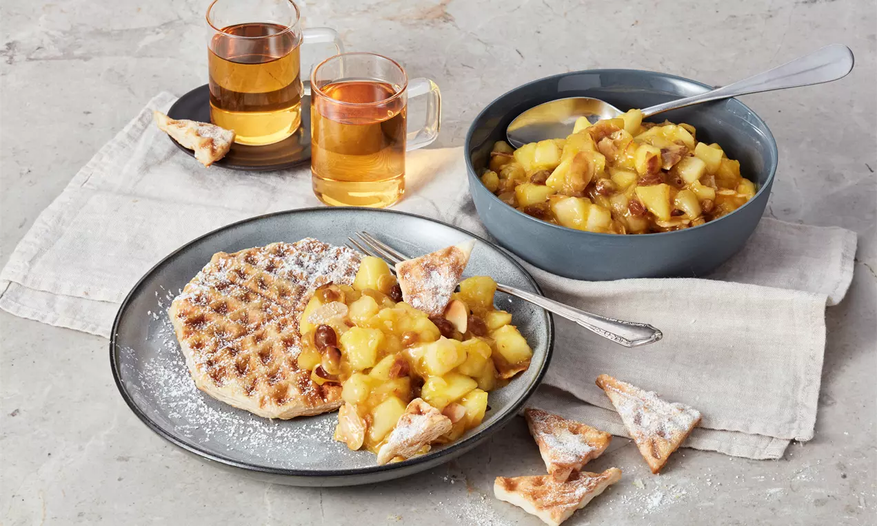 Blätterteig-Waffeln goldbraun auf weißem Teller, mit Apfel-Zimt-Rosinen-Kompott, Puderzucker bestäubt und Minzblatt garniert