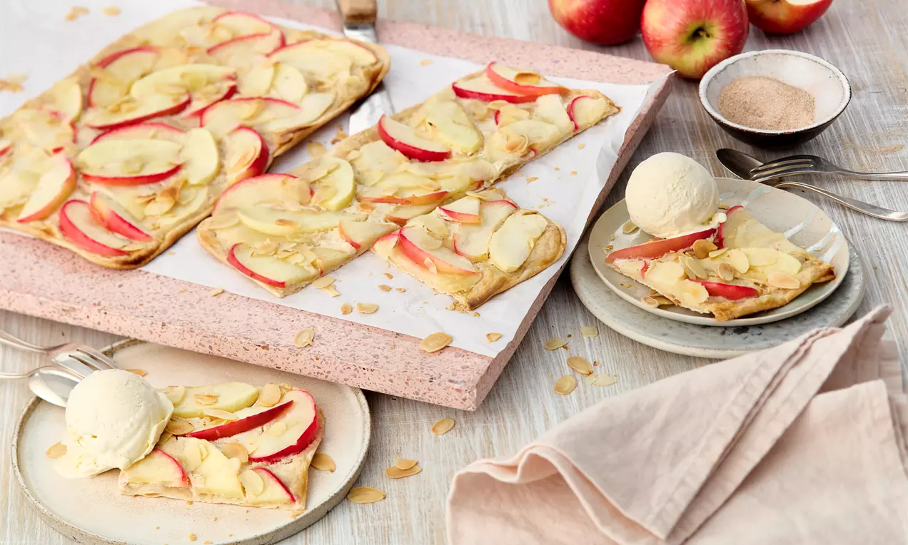 Stücke auf Brett und Tellern mit Kugel Eis: Süßer Flammkuchen mit knusprigem Teig, Apfelscheiben, Vanillecreme, Zimt und Mandeln – einfaches Rezept für herbstliche Genussmomente direkt aus dem Ofen.