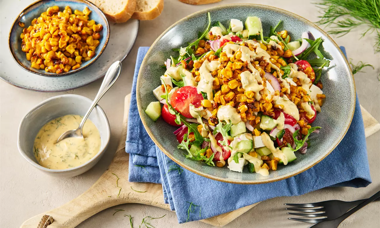 Bunter Maissalat mit goldbraun gerösteten Maiskernen, knackigem Gemüse und cremigem Dressing auf einem grauen Teller mit Brot und Kräuterdeko