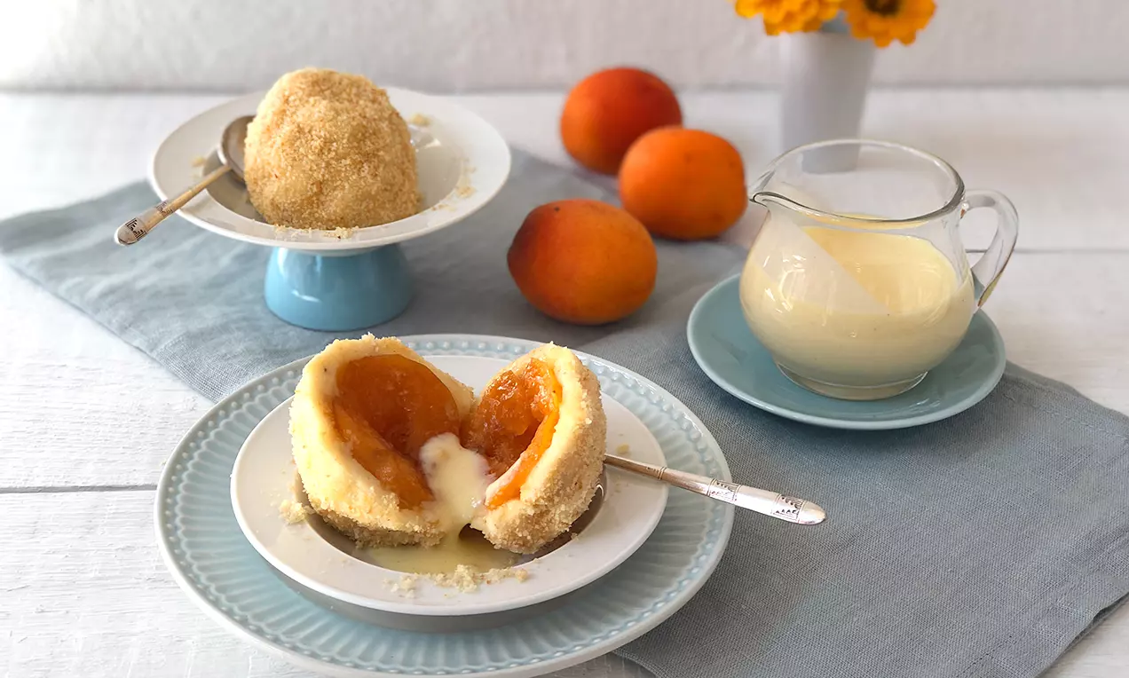Ein halbierter Topfen-Marillen-Knödel mit goldbrauner Bröselhülle, weicher Füllung aus saftigen Aprillen, angerichtet auf einem weißen Teller