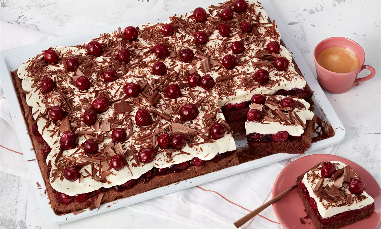Schwarzwälder Kirschtorte vom Blech mit saftigem Schokoboden, weißen Sahnetupfen, glänzenden roten Kirschen und dunklen Schokospänen